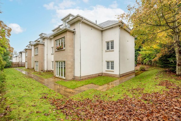 A modern residential building with a symmetrical design, featuring a central entrance, multiple windows, and a well-maintained lawn. - New Park Place Apartments (No 15) (St Andrews)