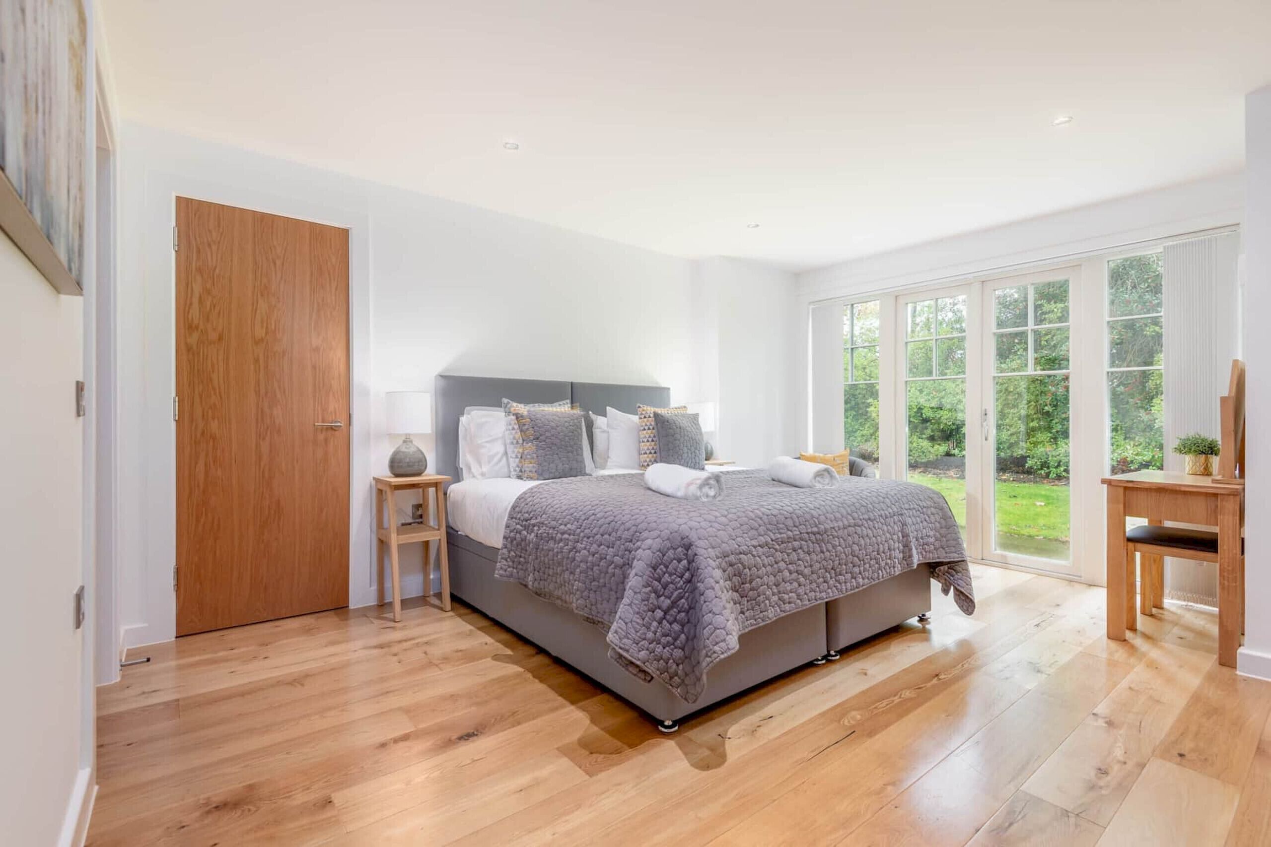Une chambre à coucher avec un lit, des tables de chevet, une porte en bois et de grandes fenêtres.