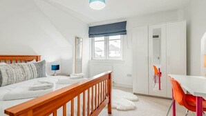 A bedroom with a bed, a nightstand, a window with a view, a wardrobe, and a desk with a chair. - Bridge Street Apartment (No 82) (St Andrews)