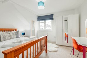 Een slaapkamer met een bed, nachtkastje, raam met uitzicht, kledingkast en bureau met stoel.