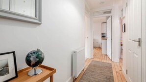 A hallway with white walls, a globe on a wooden table, and a radiator. - Bridge Street Apartment (No 82) (St Andrews)