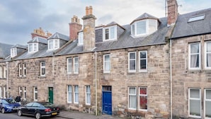 A row of stone terraced houses with uniform windows and doors, a clear sky, and parked cars on the street. - Bridge Street Apartment (No 82) (St Andrews)
