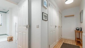 A hallway with white doors, a small wooden stool, a framed picture on the wall, and a shelf with a globe and picture frame. - Bridge Street Apartment (No 82) (St Andrews)