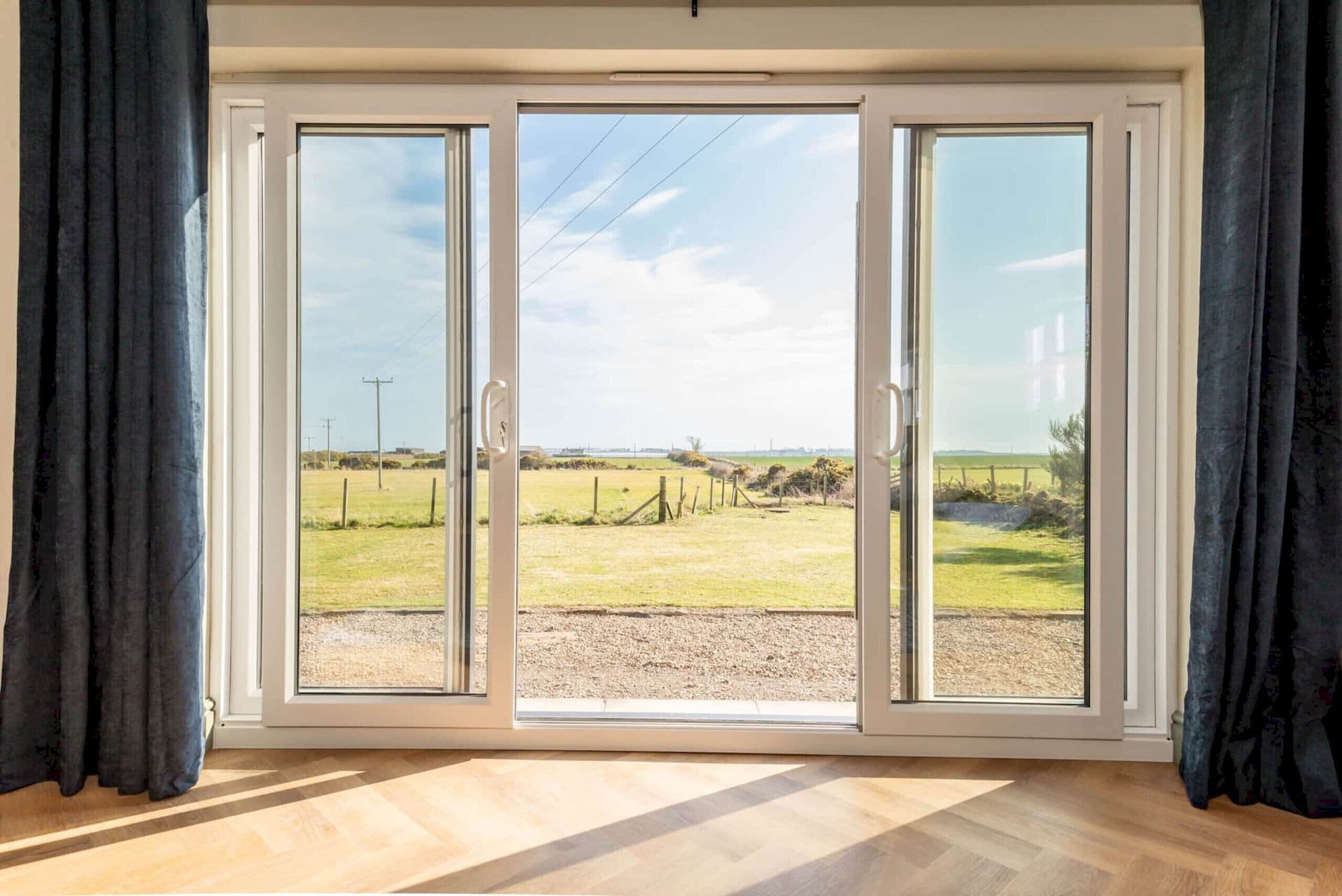 Une pièce dotée d’une grande porte-fenêtre coulissante qui donne sur un espace extérieur offrant une vue sur un champ verdoyant et une clôture.
