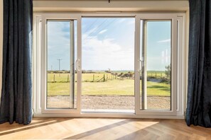 A room with a large sliding glass door leading to a grassy outdoor area. - Firthview | Crail (Anstruther)