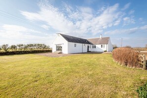 A white single-story house with a sloped roof, a front porch, and a small front yard. - Firthview | Crail (Anstruther)