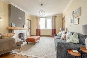 A living room with a grey sofa, a beige sofa, a wooden coffee table, a patterned rug, and a hanging light fixture. - Firthview | Crail (Anstruther)
