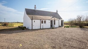 A white single-story house with a sloped roof, a front door, and a small porch area. - Firthview | Crail (Anstruther)