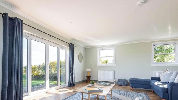 A modern living room with a flat-screen TV, a blue sofa, a coffee table, and a view of a garden through large windows.