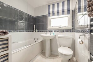 Ein Badezimmer mit Badewanne, Waschbecken und Toilette, mit blau-weißen Fliesen und einem gestreiften Vorhang.