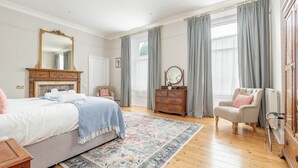 A spacious bedroom with a large bed, a wooden dresser, a chair, and a mirror. - Greyfriars Bothy (St Andrews)