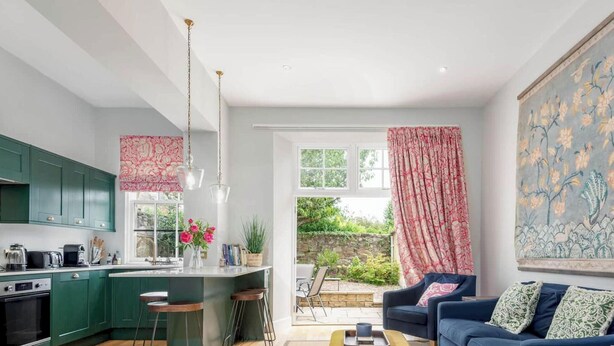 A modern kitchen with green cabinets, a dining area with a blue sofa, and a large floral painting on the wall. - Greyfriars Bothy (St Andrews)