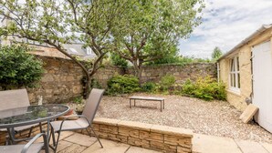A patio area with a round glass table and metal chairs, surrounded by a stone wall and a tree. - Greyfriars Bothy (St Andrews)