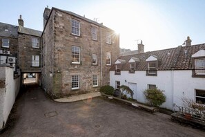 A narrow alleyway between stone buildings with a small courtyard. - The Cross Keys Apartment (85D Market Street) (St Andrews)