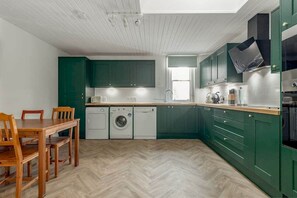 A compact kitchen with green cabinets, a wooden dining table, and a washing machine. - The Cross Keys Apartment (85D Market Street) (St Andrews)