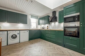 A kitchen with green cabinets, a washing machine, and a microwave. - The Cross Keys Apartment (85D Market Street) (St Andrews)