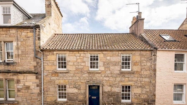 A stone building with a blue door, multiple windows, and a tiled roof. - Castle Loft (St Andrews)