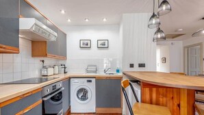A compact kitchen with a washing machine, wooden cabinets, and a bar area. - Castle Loft (St Andrews)