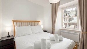 A neatly made bed with white linens and towels, a bedside lamp, and a window with curtains. - Castle Loft (St Andrews)