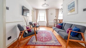 A living room with a grey sofa, a wooden chair, and a red patterned rug. - Castle Loft (St Andrews)