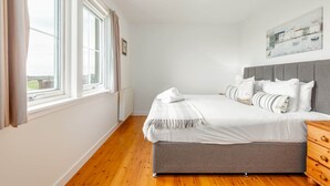 A bedroom with a bed, a dresser, a window with curtains, and a painting on the wall. - Bell Rock Cottage (St Andrews)
