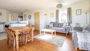 A modern living room with a grey sofa, wooden dining table, and a kitchen in the background. - Bell Rock Cottage (St Andrews)