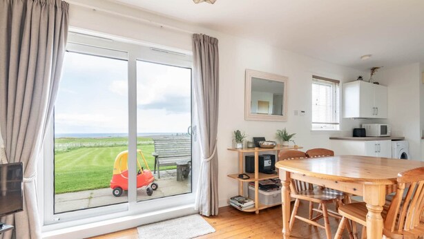 A modern kitchen with a dining area, large windows, and a view of the countryside. - Bell Rock Cottage (St Andrews)