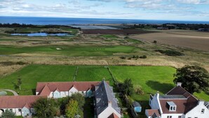 A rural landscape with a golf course, houses, and a body of water. - Bell Rock Cottage (St Andrews)