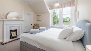 Een slaapkamer met een groot bed, een open haard en een raam met uitzicht op groen.