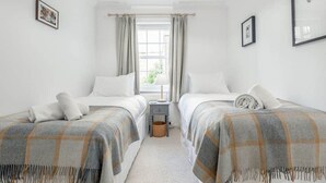 Een kamer met twee bedden, een klein tafeltje, een lamp en een raam met gordijnen.