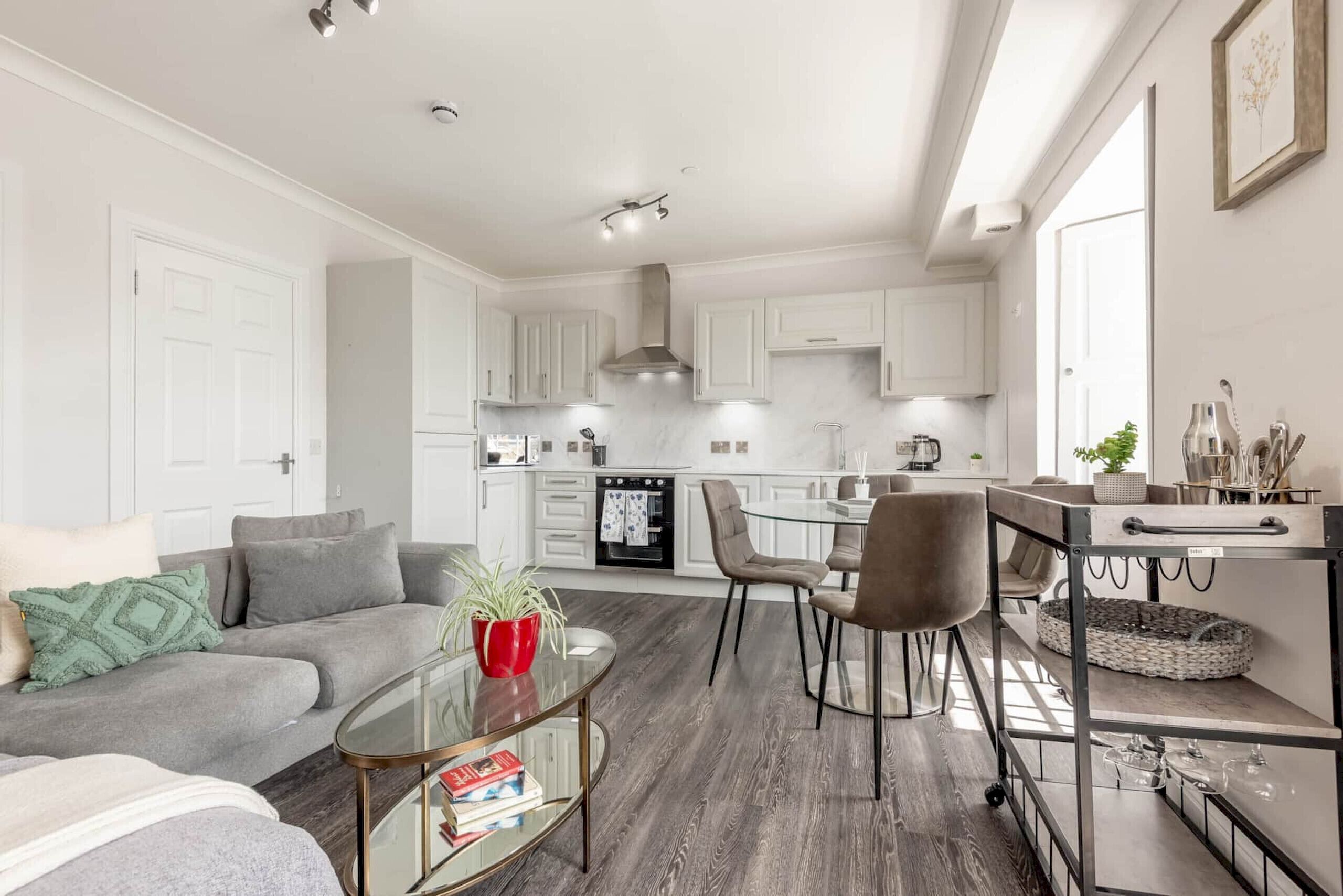 Een moderne woonkamer met een grijze bank, een glazen salontafel en een eethoek met een ronde tafel en stoelen.