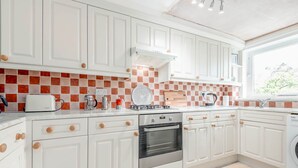 A modern kitchen with white cabinets, a built-in oven, and a window providing natural light. - The Cooperage Garden Apartment | Crail (Crail)