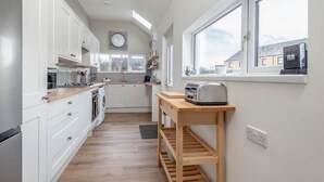 Une cuisine moderne avec des armoires blanches, un plan de travail en bois, un four encastré et une fenêtre donnant sur l’extérieur.