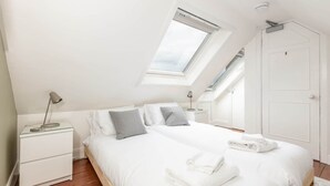 Une chambre avec un puits de lumière, un lit avec une literie blanche, une table de chevet et une armoire.