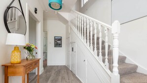 Un couloir avec une console en bois, un miroir et un escalier doté de balustrades blanches.