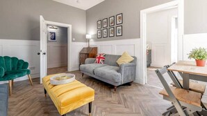 A living room with a grey sofa, a yellow ottoman, a green armchair, and a dining area with a table and chairs. - The Doctor's House (St Andrews)