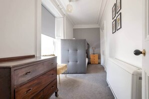 Um corredor estreito com um aparador de madeira, uma poltrona cinza com textura aveludada e um radiador branco.