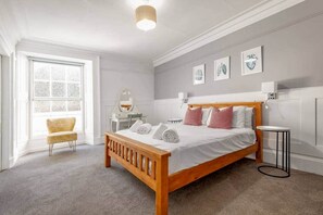 A bedroom with a wooden bed, a chair, a bedside table, a mirror, and artwork on the wall. - The Doctor's House (St Andrews)