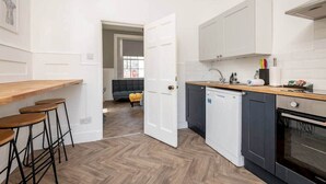 A compact kitchen with a wooden countertop, bar stools, a dishwasher, and a dark-colored oven. - The Doctor's House (St Andrews)