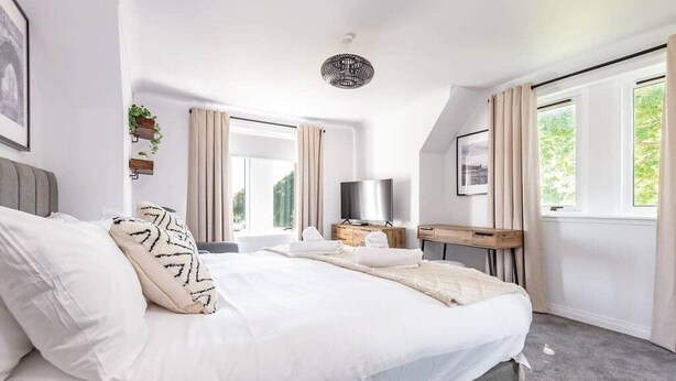 A modern bedroom with a large bed, a desk, a TV, and a window with curtains. - Abbey Villa (No 6) (St Andrews)
