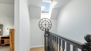 A staircase with a black railing, a wooden floor, and a large wall clock. - Abbey Villa (No 6) (St Andrews)