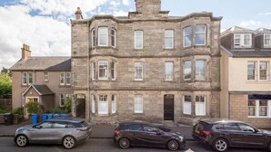 A multi-story stone building with a traditional architectural style, featuring a central entrance with a black door, and a row of windows on the ground floor. - Argyle Street Apartment (No 44) (St Andrews)