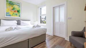 A bedroom with a bed, a gray sofa, a window, and a door. - Argyle Street Apartment (No 44) (St Andrews)