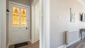 A hallway with a white door featuring decorative glass panels, a radiator on the wall, and a small plant on the left. - Argyle Street Apartment (No 44) (St Andrews)