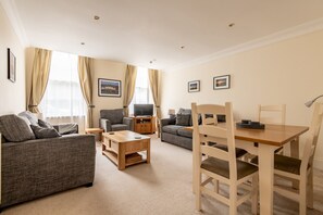 A living room with two sofas, a wooden coffee table, a TV, and a dining table with chairs.