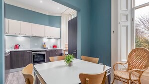 A modern kitchen with white cabinets, a dining table with chairs, and a view of the outdoors. - Queen's Gardens (No 18B) (St Andrews)