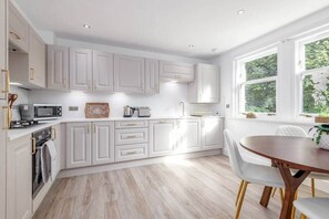 Una cocina moderna con armarios blancos, una zona de comedor con mesa de madera y una ventana que proporciona luz natural.