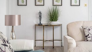 Een woonkamer met een bank, een lamp, een bijzettafeltje met een plant en lijstwerken aan de muur.