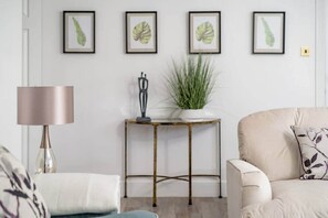 Una sala de estar con un sofá, una mesa con una planta y obras de arte enmarcadas en la pared.