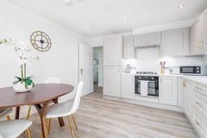 Una cocina moderna con armarios blancos, una mesa de comedor de madera con sillas blancas y un reloj en la pared.